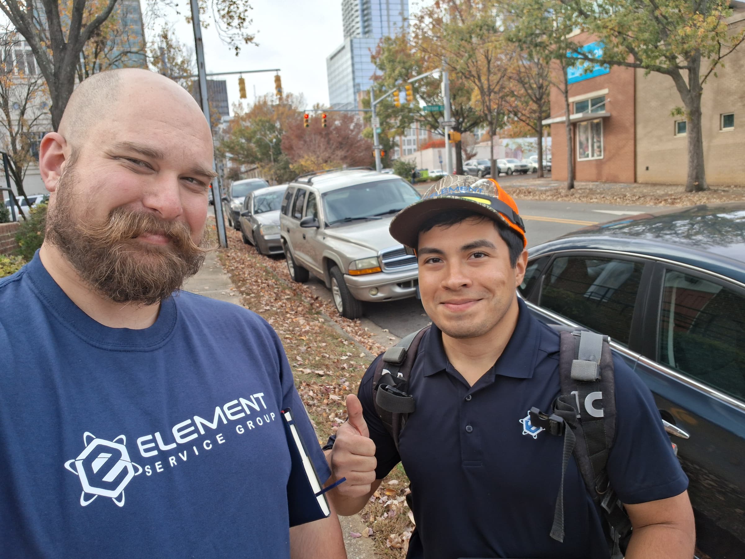Two HVAC technicians smiling outdoors, showcasing professionalism and teamwork in urban setting.