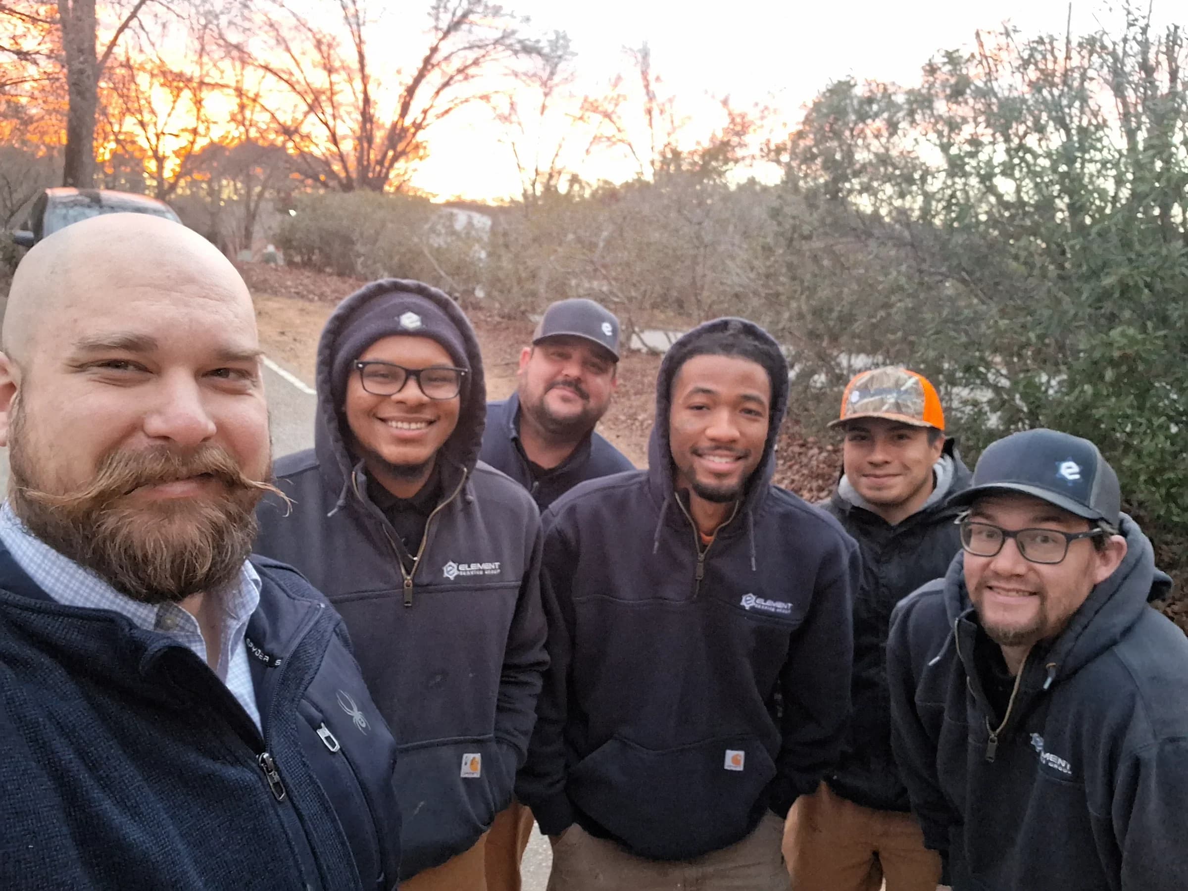 HVAC and plumbing team posing outdoors at sunset, showcasing professionalism and camaraderie.